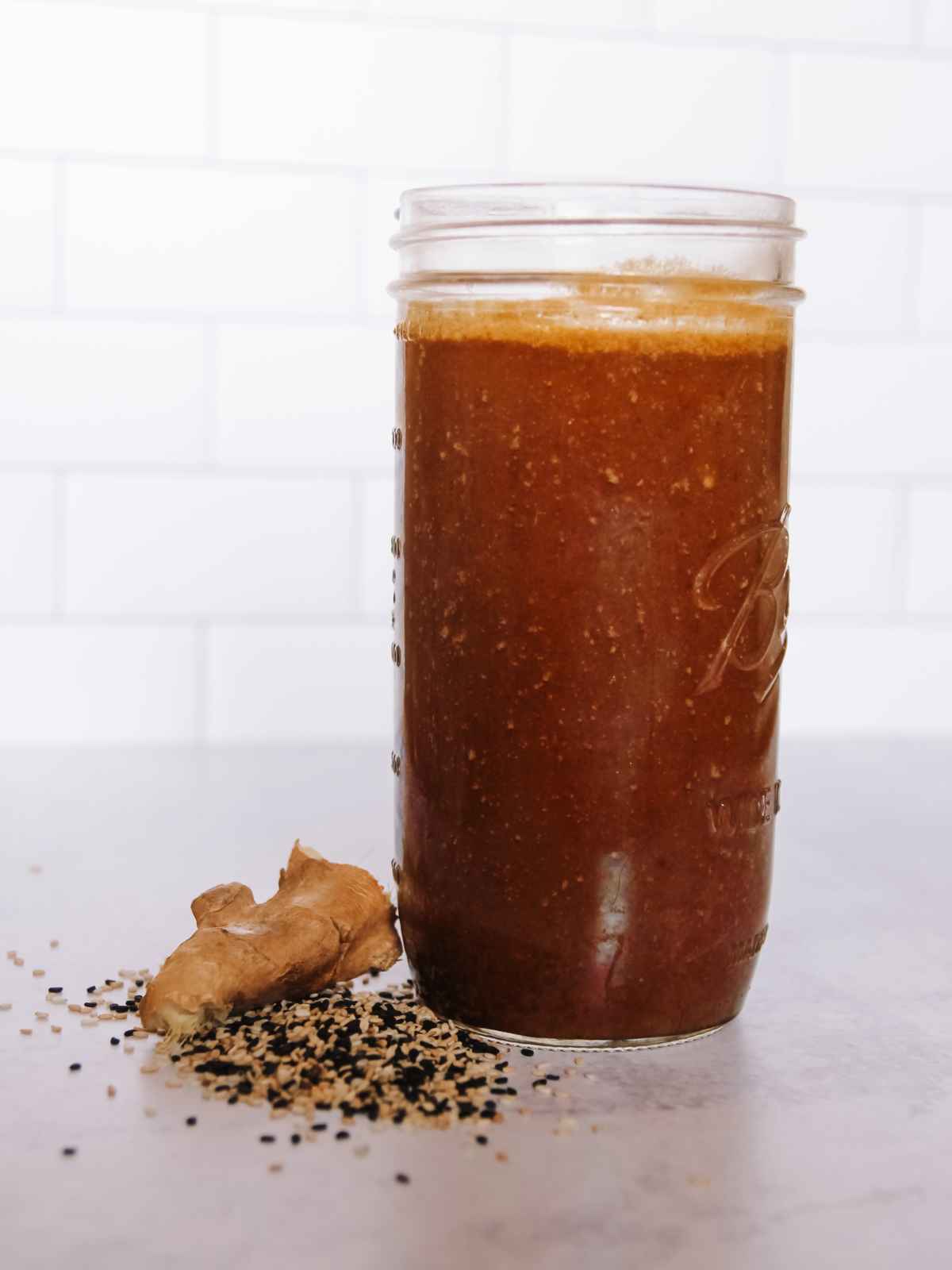 mason jar full of vegan teriyaki sauce with a knob of ginger and some sesame seeds next to it