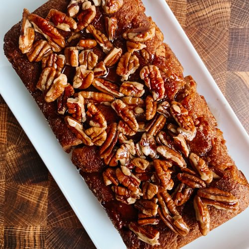 a loaf of pecan breakfast bread on a white rectangular platter